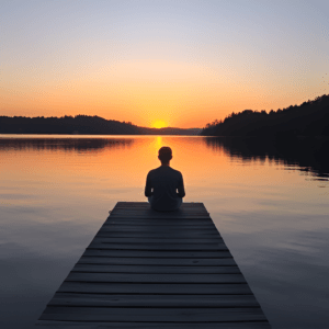 A person sitting on a dock, looking at a peaceful lake at sunrise.
