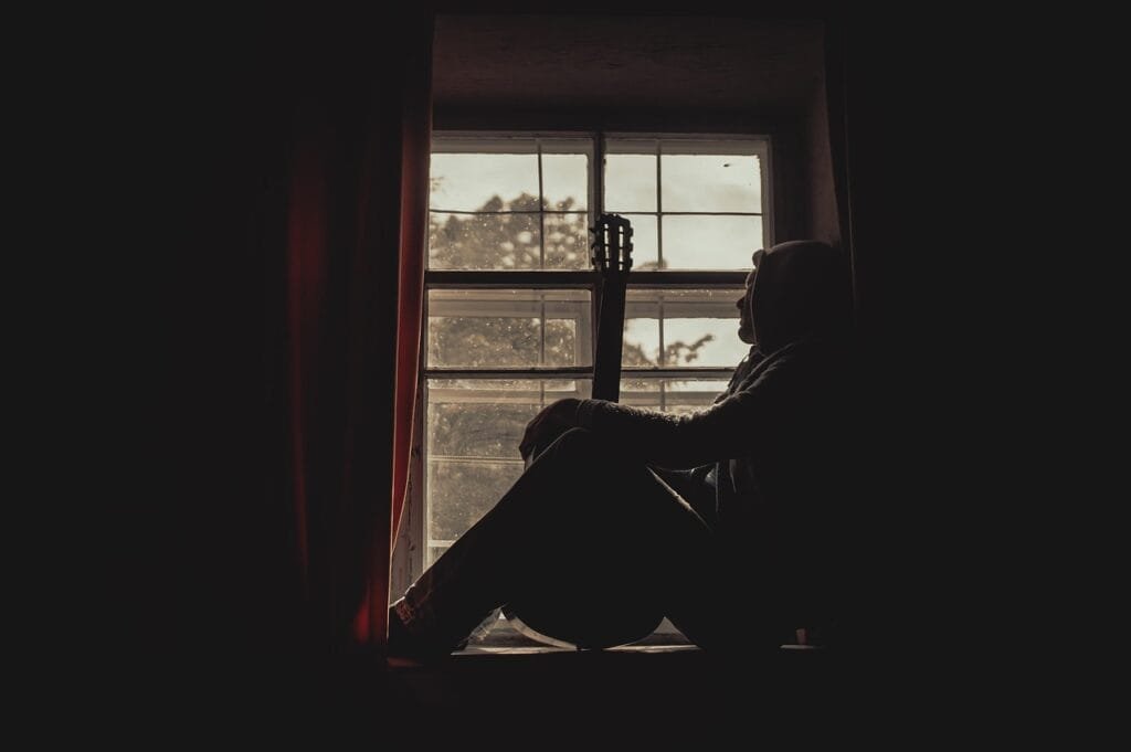 man sitting on the window with his guitar looking out. social anxiety, human, thoughtful, silhouette, invisible illness, mental health