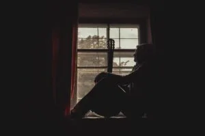 man sitting on the window with his guitar looking out. social anxiety, human, thoughtful, silhouette, invisible illness, mental health