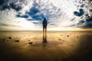 A lone figure stands on a tranquil beach during a vivid sunset, reflecting on the wet sand. insecurity, attention seeking,