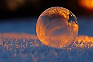 Close-up shot of a frozen bubble with warm reflections resting on a snowy surface at twilight.