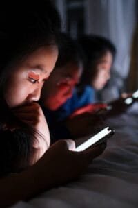 Three teenagers using smartphones in bed at night, highlighting modern digital habits.