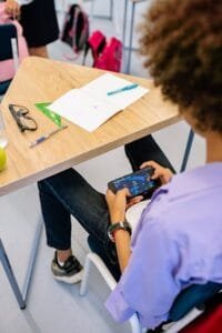 A student engaging with a smartphone game during class, captured indoors. A student engaging with a smartphone.