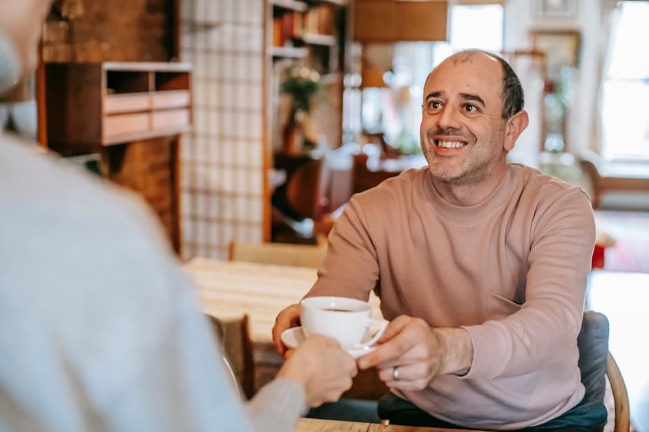 Happy middle-aged man receiving a cup of coffee from a partner in a warm, cozy home kitchen. people pleaser, conditional love